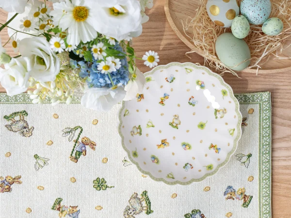 Plate with Easter decorations from Easter Delight on an Easter-inspired table A deep plate with bunny and flower decorations from Easter Delight on a patterned placemat next to a bouquet of flowers and a basket of pastel-colored Easter eggs.