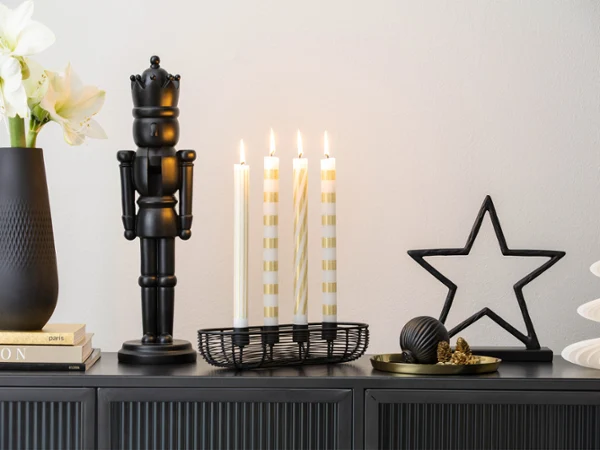 A dark vase, a black nutcracker, four lit candles, star-shaped decorations and small ornaments arranged on a cupboard.