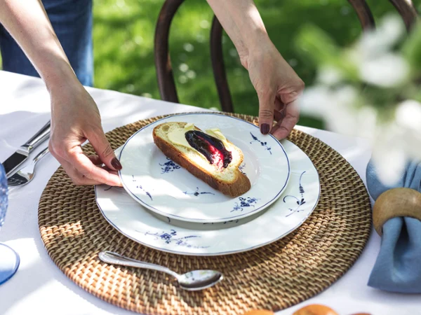 A person places an Old Luxembourg plate on a table A person places an Old Luxembourg plate, topped with fruit spread and butter, on a woven placemat.