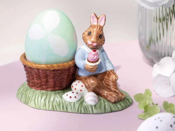 Ceramic Annual Easter Edition 2026 bunny figurine Ceramic Annual Easter Edition 2026 bunny figurine in a blue jacket sits beside a large pastel egg in a basket on a grassy base with small eggs.