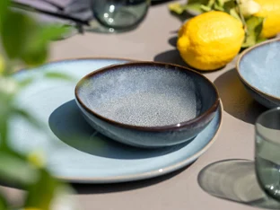 Lave plate and bowl on a table with lemons Blue ceramic bowl and plate on a table with glasses, lemons and green plants in the background.