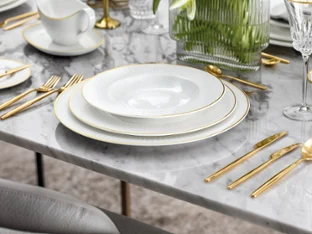 Elegant table setting with white Château Septfontaines plates, golden MetroChic d’Or flatware and crystal glasses on a marble table.