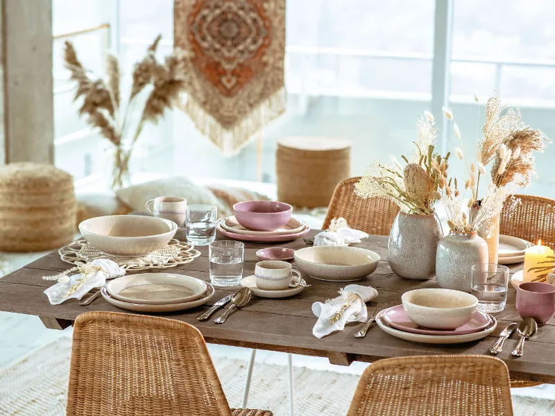 A dining table with rattan chairs and wicker baskets set with like. by Villeroy & Boch Perlemor tableware.