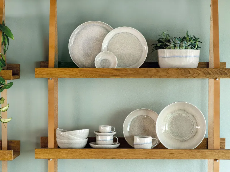 A wooden shelf with beige plates and bowls from the Perlemor collection.