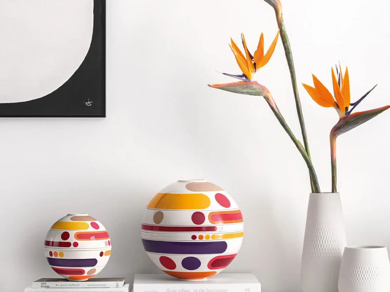 A minimalist sideboard showcases the modern La Boule Miami, vases, bird of paradise flowers, and stacked books under abstract wall art.
