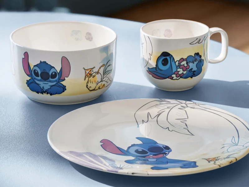 Un cuenco, una taza y un plato con el personaje azul de dibujos animados Stitch. Un cuenco, una taza y un plato con el personaje de dibujos animados azul Stitch sobre una mesa azul claro.