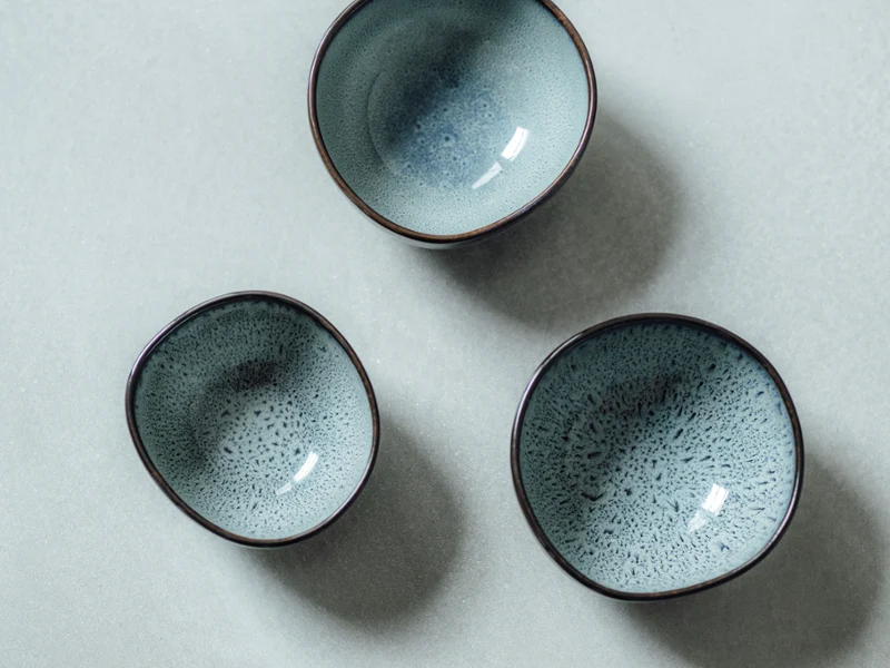 Drei leere, grau gesprenkelte Keramikschüsseln Lave Gris von Villeroy & Boch sind auf einem hellen Untergrund arrangiert.