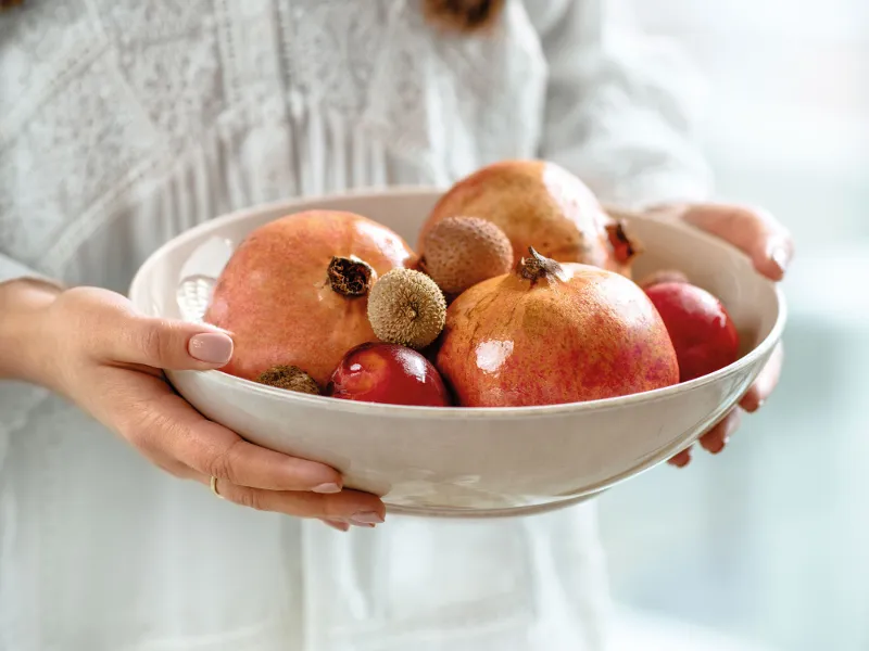 A woman holding a beige Perlemor bowl with pomegranates and lychees.