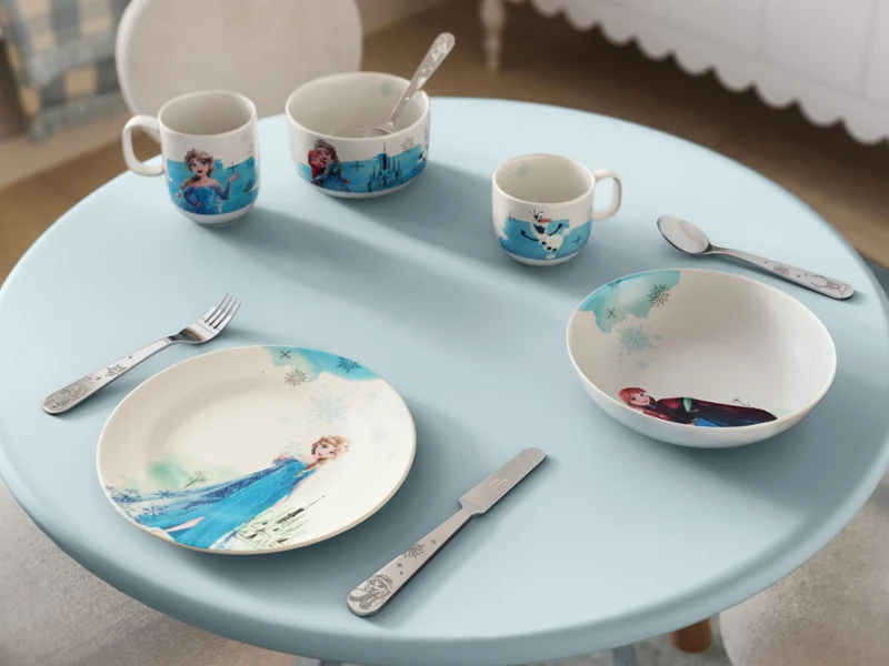 Una pequeña mesa azul con vajilla infantil de Disney Frozen. Una pequeña mesa azul con vajilla infantil de Disney Frozen, que muestra un personaje de dibujos animados, utensilios y tazas.