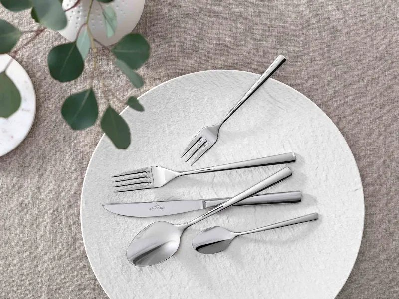 Elegant table decoration with modern Piemont cutlery and decorative greenery on a neutral tablecloth.