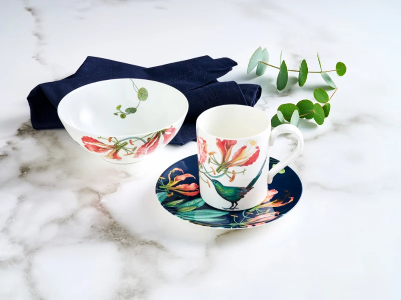 Avarua set for one, featuring a cup, saucer, and small bowl, is beautifully adorned with delicate fauna and red floral accents, and complemented by a rich dark blue napkin.