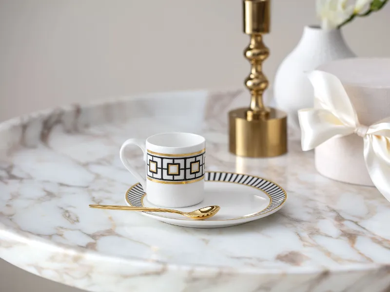 A golden MetroChic coffee cup and saucer on a marble table.