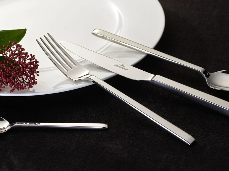 A white plate with neatly arranged silverware and a single flower placed elegantly beside it.