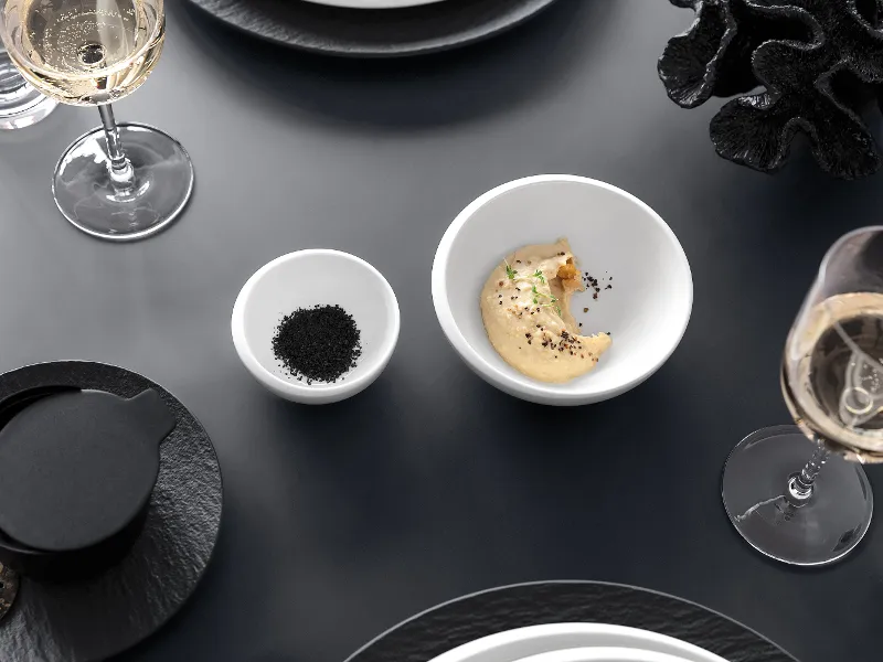 Topshot of an elegant dining room with a NewMoon bowl, a small bowl with spices and filled wine glasses on a grey table.