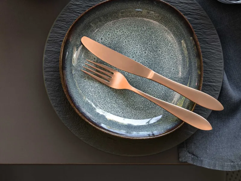 Elegant table decoration with modern Manufacture and Lave crockery and copper cutlery from the Manufacture collection on a dark tablecloth.