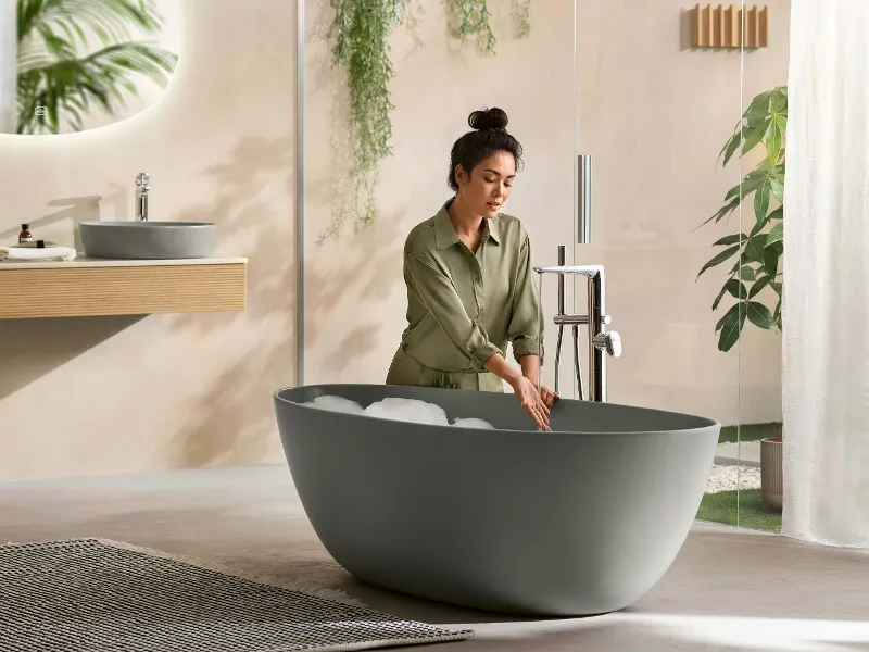 A woman pouring bubble bath into a green freestanding Antao bath.