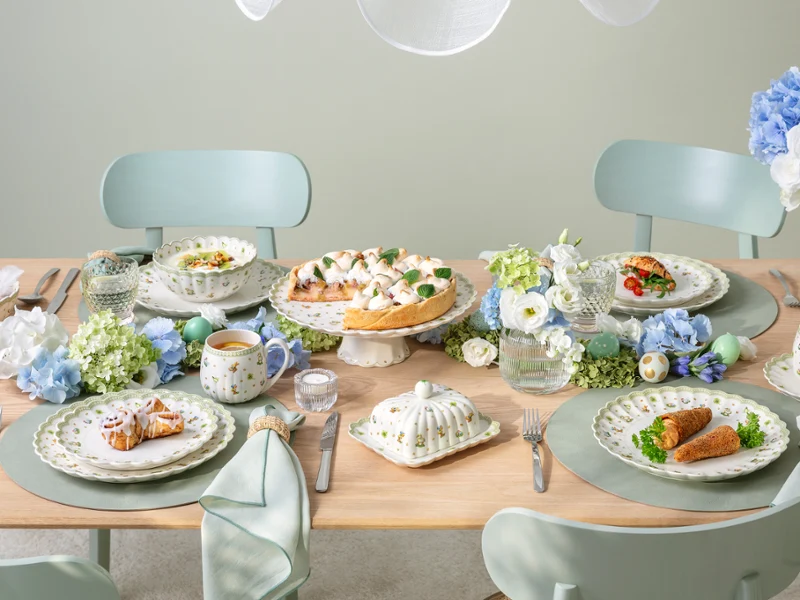 A Easter Delight dining table set for four with Easter Delight decorations, pastel tableware, and plates of food arranged neatly.