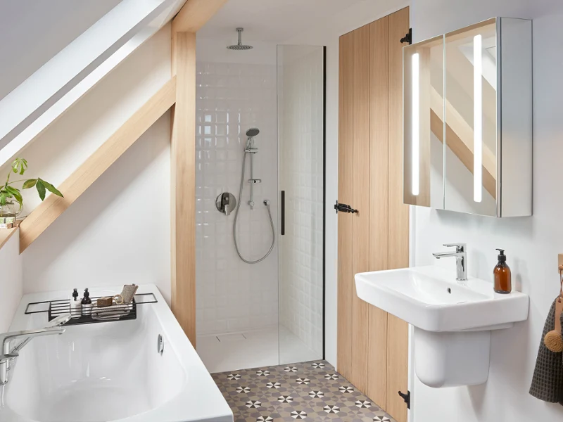 Modern bathroom with a shower, a washbasin and a bath under a sloping ceiling A modern bathroom with a walk-in shower, a white washbasin, a mirror cabinet and a bath under a sloping ceiling. The floor is tiled with a geometric pattern. A wooden door and beams accentuate the room.
