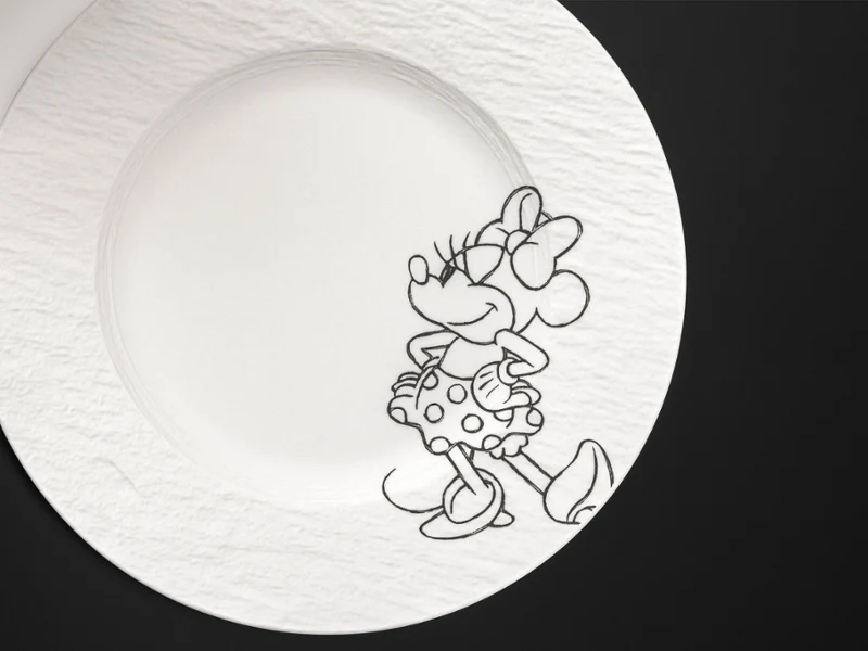 Plato blanco Manufacture Disney con el contorno negro de un ratón de dibujos animados. Plato blanco Manufacture Disney con el contorno negro de un ratón de dibujos animados sobre fondo negro.