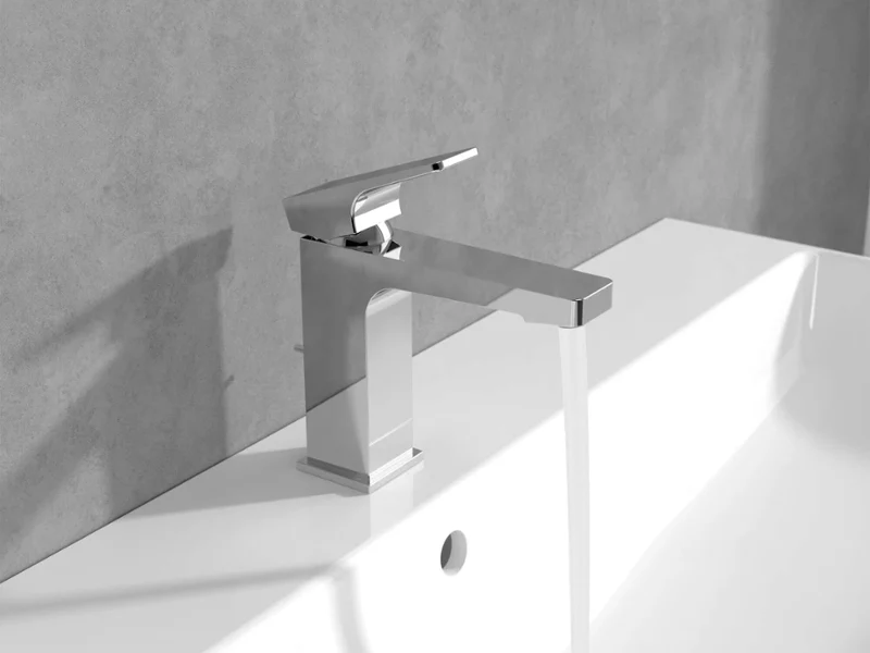 Chromowana bateria Architectura Square na białej umywalce Nowoczesna chromowana bateria, z której woda spływa do białej umywalki na tle szarej ściany.