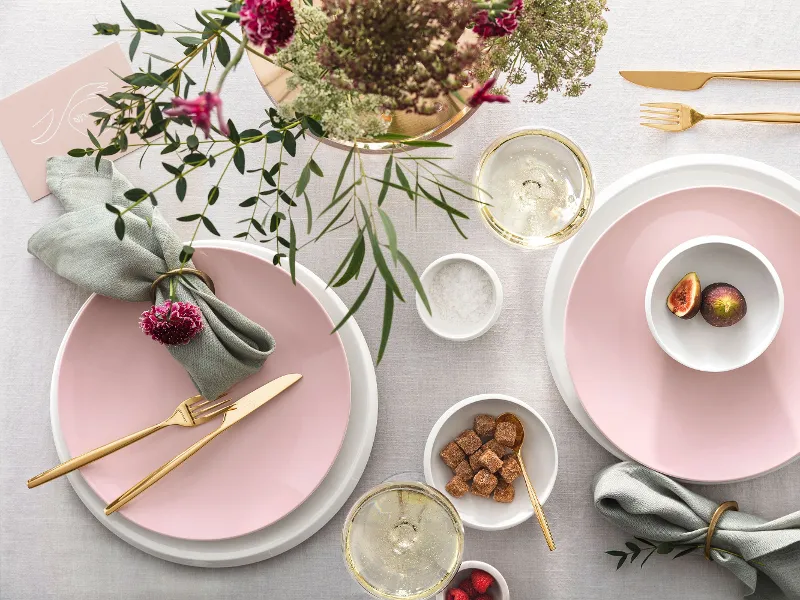 Elegant table decoration with pink Rose Garden plates, gold MetroChic cutlery, fresh flowers and a touch of green, along with drinks and light snacks.