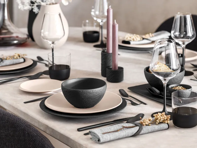 A table set with black Manufacture and beige NewMoon plates and black cutlery.