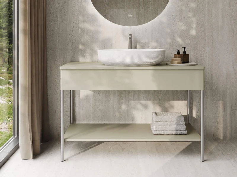 Modern bathroom with a round mirror, a countertop washbasin, a white vanity unit, and folded towels, located next to a large window with curtains.