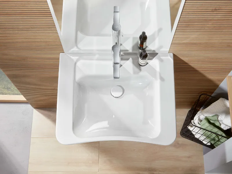 Lavabo rettangolare bianco con rubinetto, dispenser di sapone e un cesto con asciugamani nelle vicinanze, visto dall'alto.
