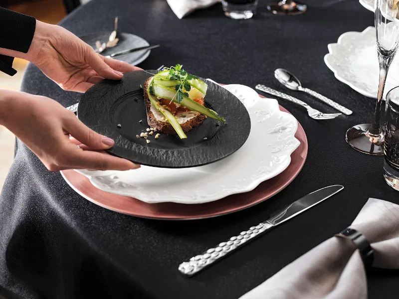 A woman serving the starter at a Christmas table set with white Toy's Delight and black Manufacture plates.