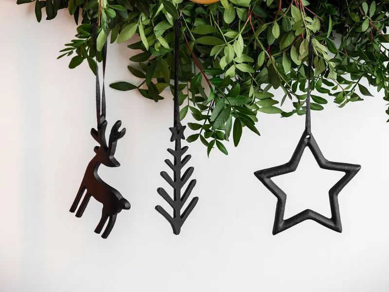 Green door wreath decorated with hanging Black XMAS ornaments in front of a white wall.