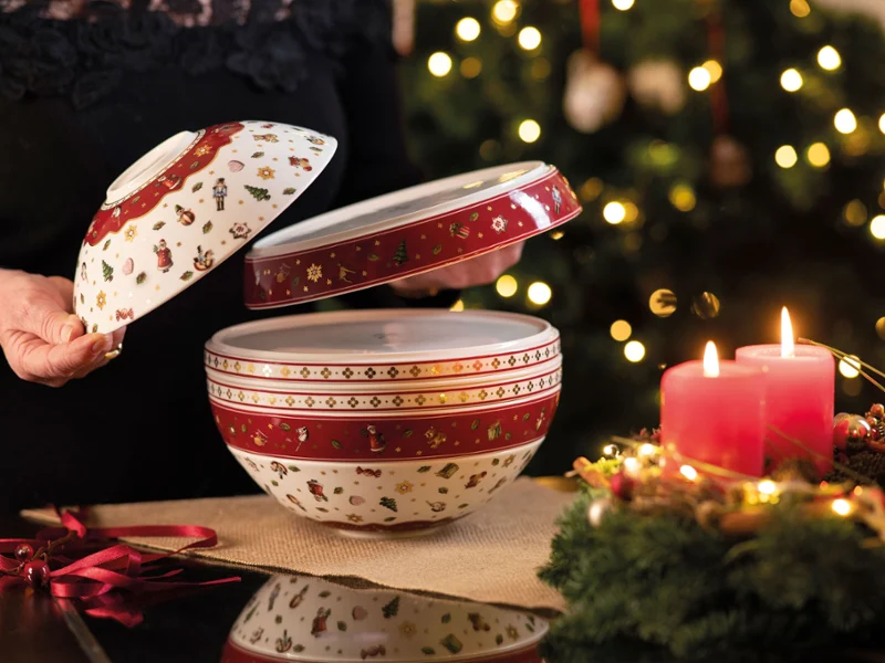 Seven-piece dinner set being unpacked Person opening a decorative dinner set, next to burning red candles and a Christmas tree with lights in the background.