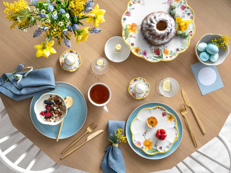 A springtime table setting with Spring Awakening and Crafted dinnerware, a Bundt cake, a serving bowl of oatmeal with berries, a cup of tea and decorative eggs.