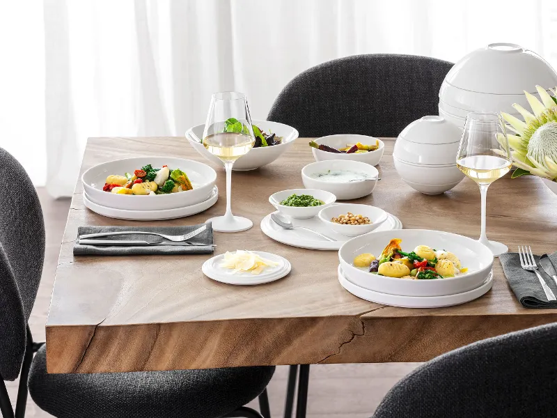 A La Boule table setting with two plates of food, two glasses of white wine, various bowls with side dishes and a flower arrangement with black and grey chairs around the table.