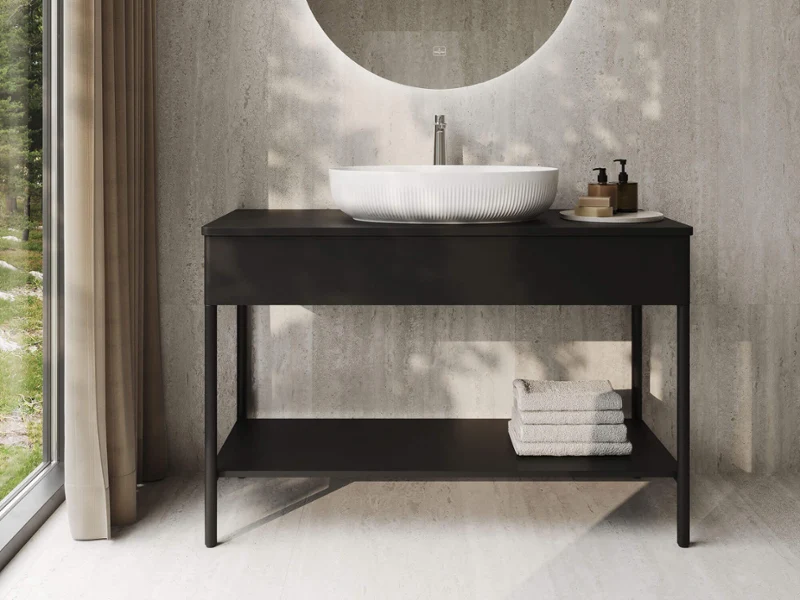 Modern bathroom with a round mirror, a countertop washbasin, a black vanity unit, and folded towels, located next to a large window with curtains.
