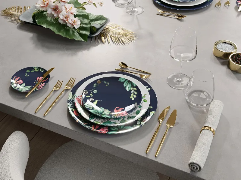 Ein formelles Tischgedeck mit Avarua Tellern und MetroChic Besteck Ein formelles Tischgedeck mit Blumentellern, goldenem Besteck, Glaswaren, einer Serviette und einem Blumengesteck in der Mitte.