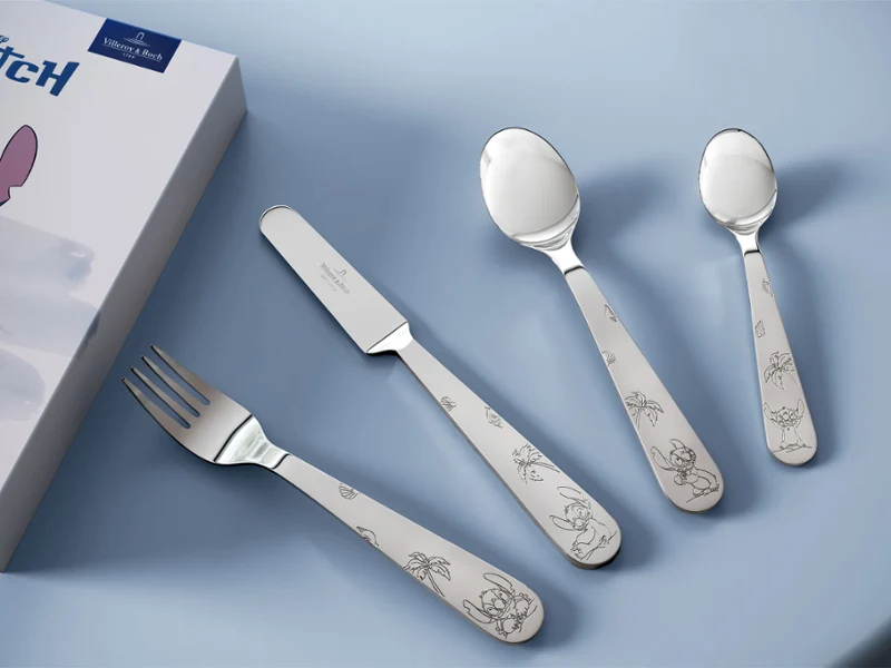 Juego de cubertería de cuatro piezas de acero inoxidable con mangos de la colección Disney Stitch. La caja del juego de cubertería de cuatro piezas de acero inoxidable con mangos de la colección Disney Stitch sobre una superficie azul claro.