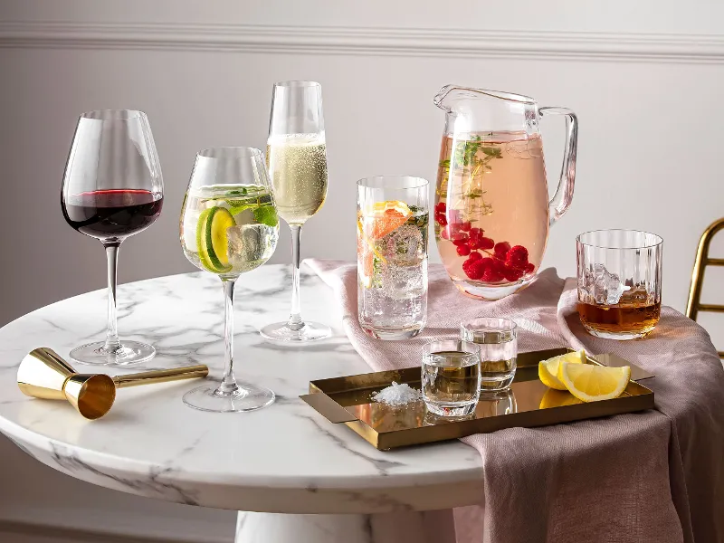 Glasses and jugs from the Villeroy & Boch Rose Garden collection on a round marble table with drinks and citrus fruits.