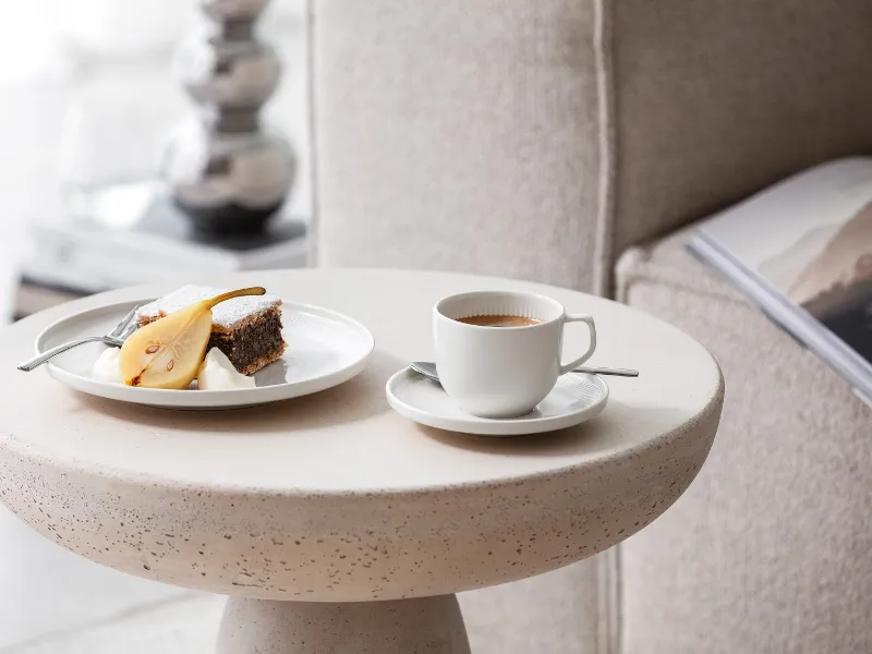 A cup of coffee and a plate of cakes served on a modern side table with Afina crockery from Villeroy & Boch.