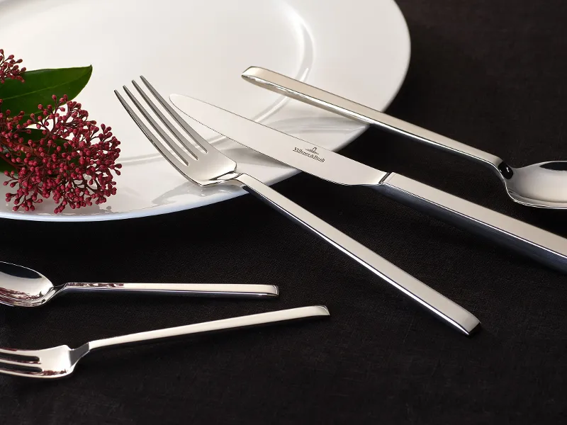 Shiny La Classica cutlery and a decorative flower on a white plate against a dark background.