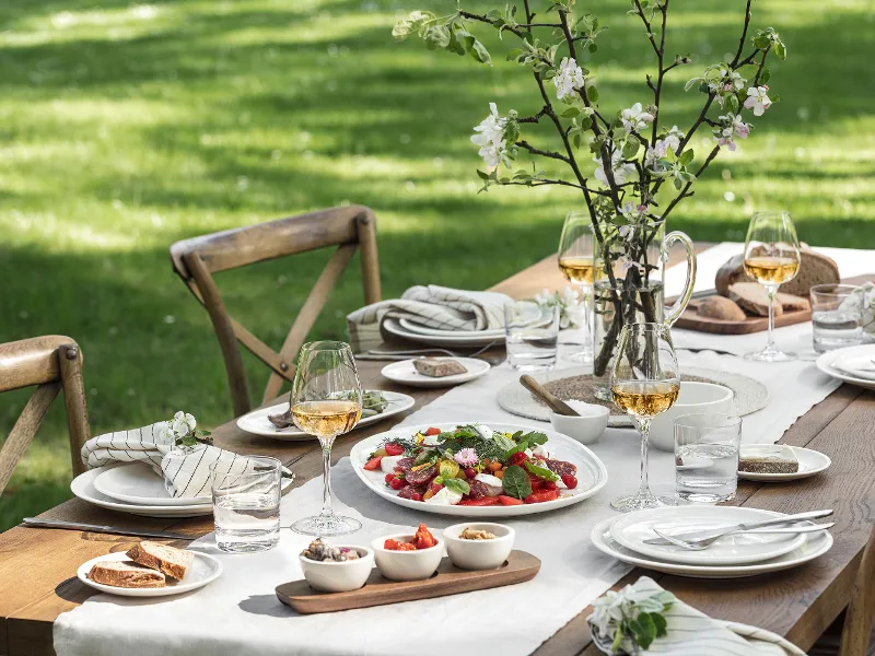 Outdoor table setting with Villeroy & Boch Artesano crockery, fresh salads, glasses and a flower vase.