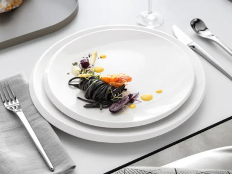 Un’elegante mise en place con piatti bianchi e pietanze della collezione NewMoon, armoniosamente disposti con posate.


