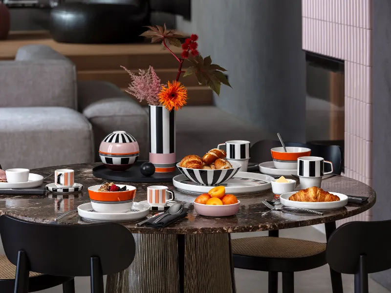 Ein runder, zum Frühstück gedeckter Tisch mit Croissants, Obst, Kaffee und schwarz-weiß gestreiftem Geschirr aus der Kollektion Memphis von Villeroy & Boch.