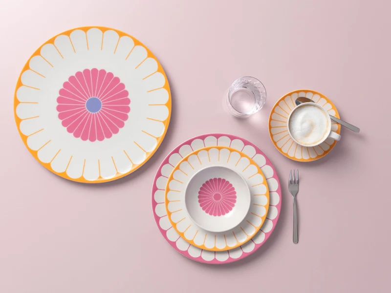 Four plates with a floral pattern, a cup and saucer, a water glass and a fork on a light pink surface.