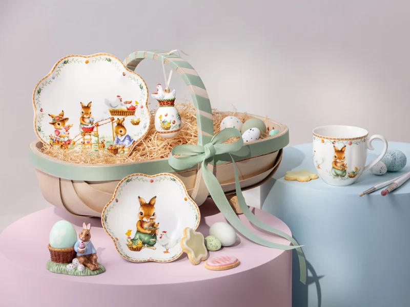 Annual Easter Edition 2026 tableware with bunny designs, eggs, a mug, and cookies arranged on pastel-colored platforms.