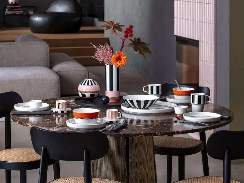 Esstisch mit schwarzen Stühlen, bunt gemustertem Memphis Geschirr, Memphis Vasen mit Blumen und zeitgenössischem Dekor in einem modernen Raum.