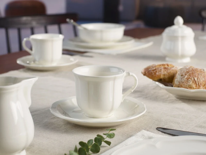 A serene breakfast table with white ceramic cups, saucers, and a sugar bowl on a light tablecloth. Fresh pastries add a warm, inviting touch.