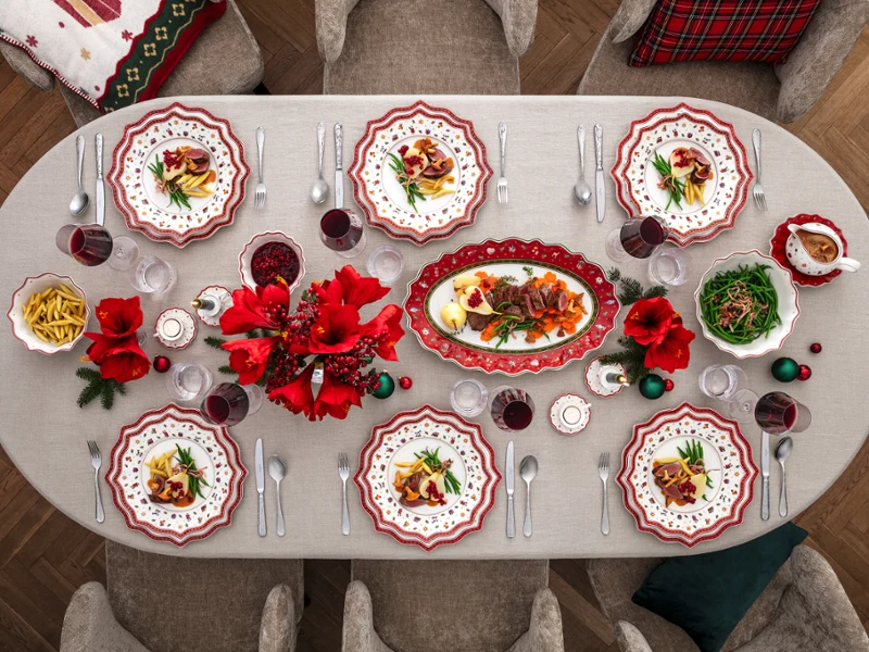 A festive dining table setting A festive dining table setting for eight people with red and white patterned plates, red flowers, glasses, cutlery and various dishes, including pasta and salad, on a white tablecloth.