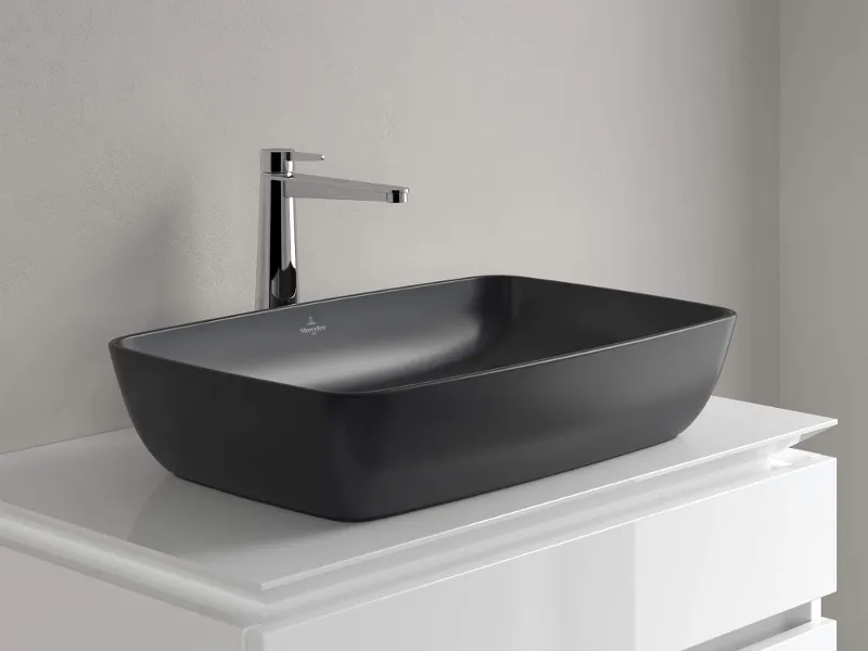 Ein schwarzes Aufsatzwaschbecken in neutralem Umfeld mit Chromarmatur auf einem weißen Unterschrank mit zwei Auszügen.