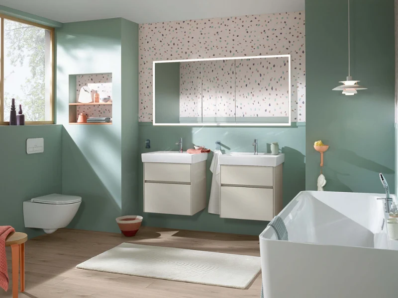 Collaro pastel bathroom with twin sinks and bath Fresh Collaro bathroom in pastel tones with twin washbasins, white bath, and terrazzo-style wall. Soft green accents and wood flooring create a cheerful, modern look.