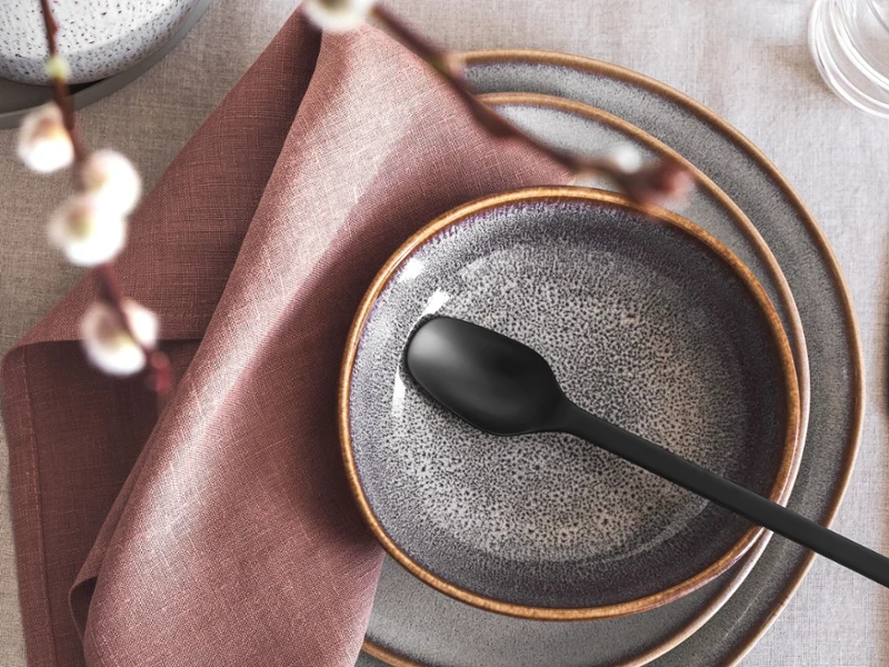 Verschiedene Größen an Tellern der Lave Kollektion in beige stehen auf einem gedeckten Tisch aufeinander. Die Deko unterstreicht den Vintage Look.